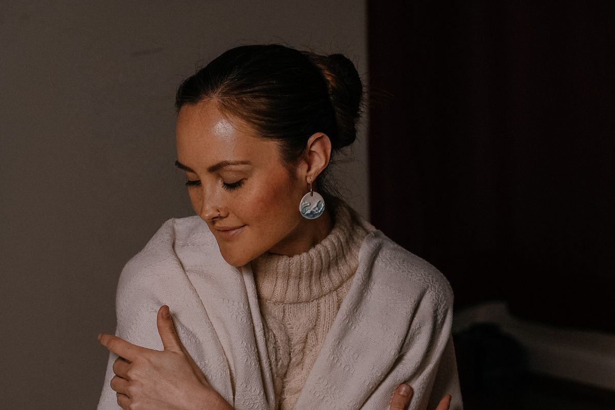Kira wrapped in a cream blanket, eyes closed, holding herself