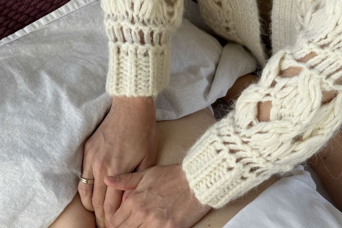 Hands resting on a client’s belly, sleeves of a cream knit cardigan