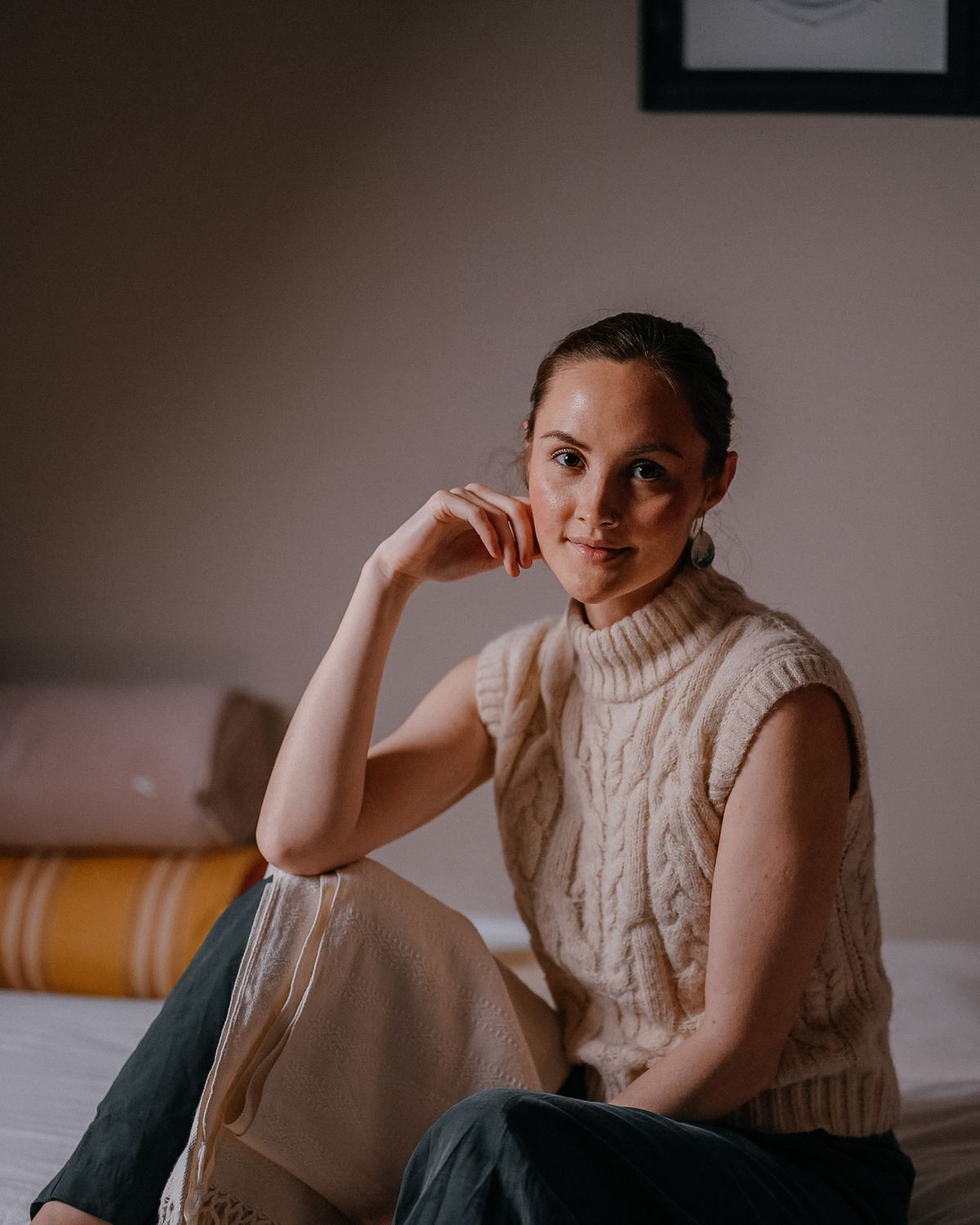 Kira Shay, seated on the massage table in a cream knit vest
